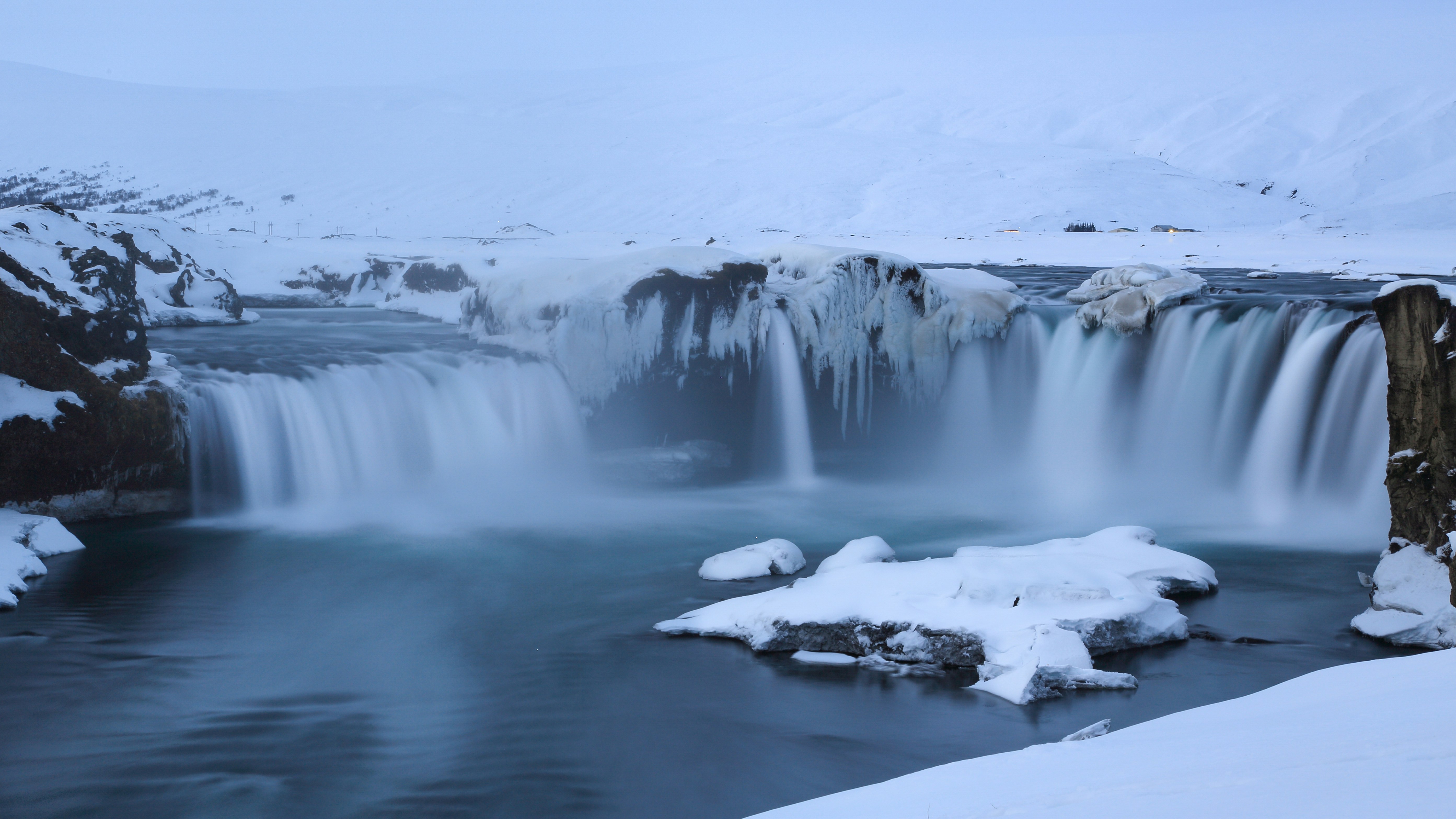 white snow on black rock formation near body of water during daytime